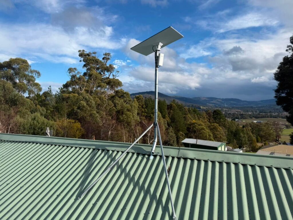Starlink dish and point to point WiFi sender on a guyed roof mast at a property in Huonville, Tasmania