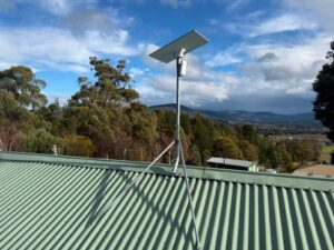 Starlink dish and point to point WiFi sender on a guyed roof mast at a property in Huonville, Tasmania