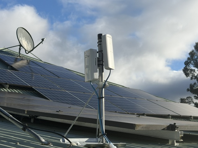 Point to point WiFi radio units on a roof mast beside solar panels in Geeveston, Tasmania